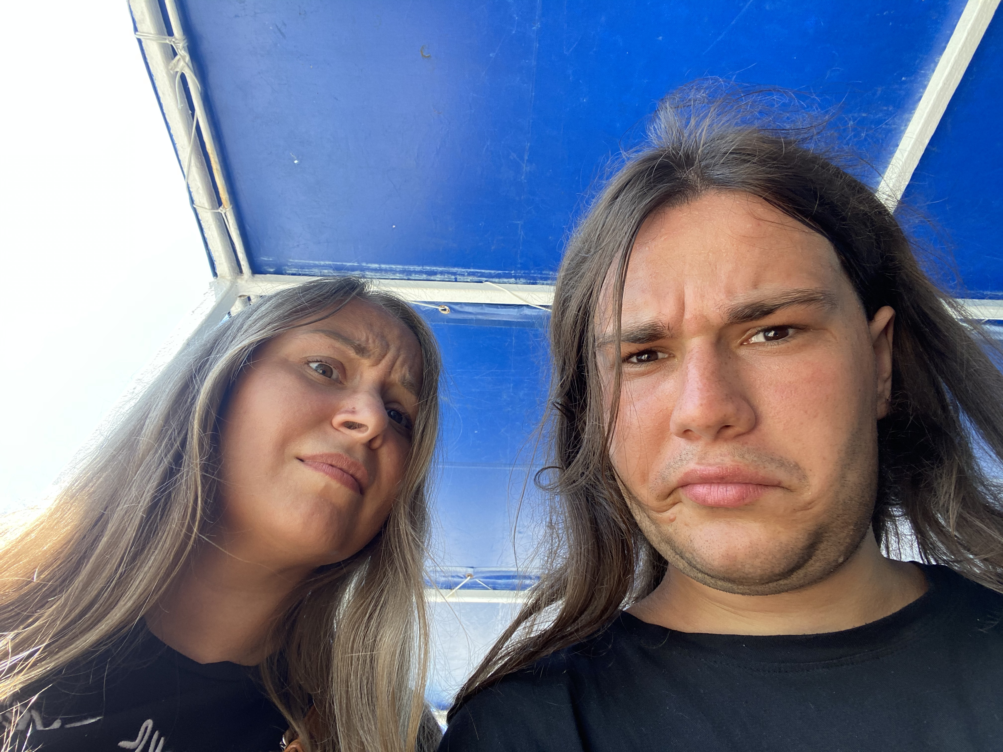 Two young people under a blue canopy looking directly at the camera against a bright backdrop